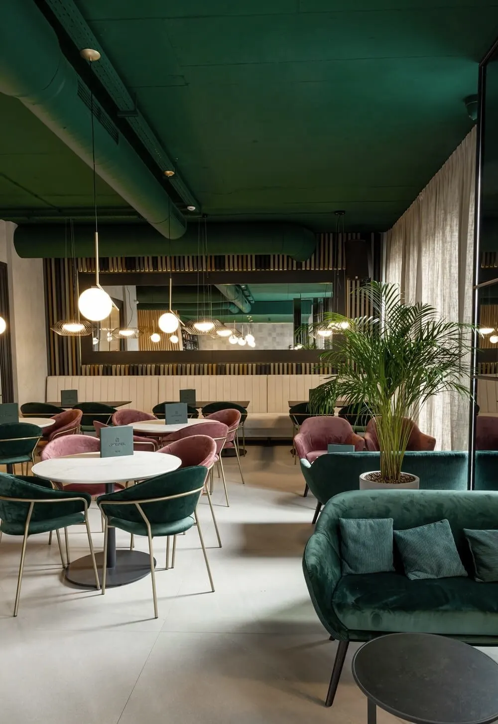 Sala restorana Akvarel sa zelenim baršunastim sofama, roze foteljama, okruglim mermernim stolovima i palmom